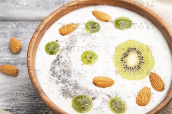 Yogurt with kiwi, gooseberry, chia and almonds in wooden bowl on gray wooden background and linen