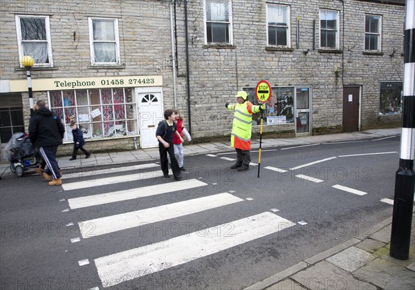 Lollipop man stopping traffic to allow people to cross the road safely, Somerton, Somerset,