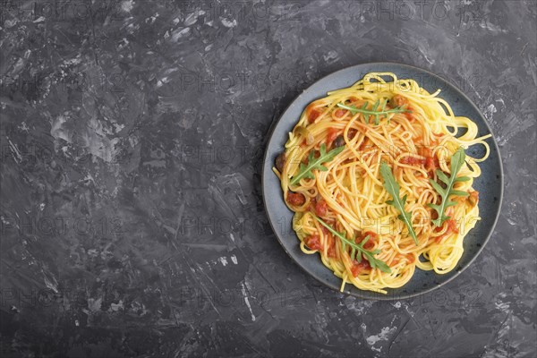 Corn noodles with tomato sauce and arugula on a black concrete background. Top view, flat lay, copy