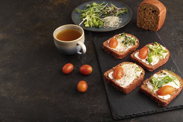 Red beet bread sandwiches with cream cheese, tomatoes and microgreen on black concrete background.