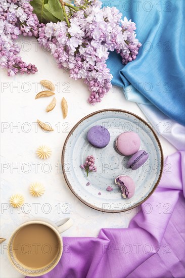 Purple macarons or macaroons cakes with cup of coffee on a white concrete background and