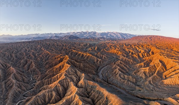 Riverbed in a landscape of eroded hills, badlands at sunrise, Issyk Kul Lake in the background,