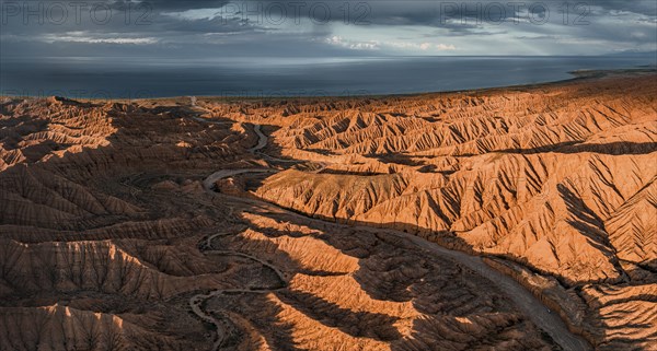 Riverbed runs through a landscape of eroded hills, badlands at sunset, Issyk Kul Lake in the