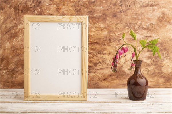Wooden frame with pink dicentra, broken heart in ceramic vase on brown concrete background. side