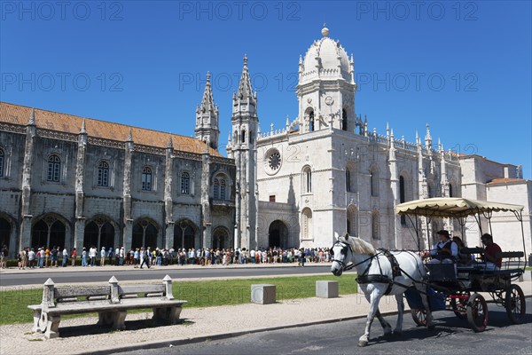 Eine gotische Kathedrale unter klarem blauen Himmel mit Touristen und einer Kutsche mit Pferden im
