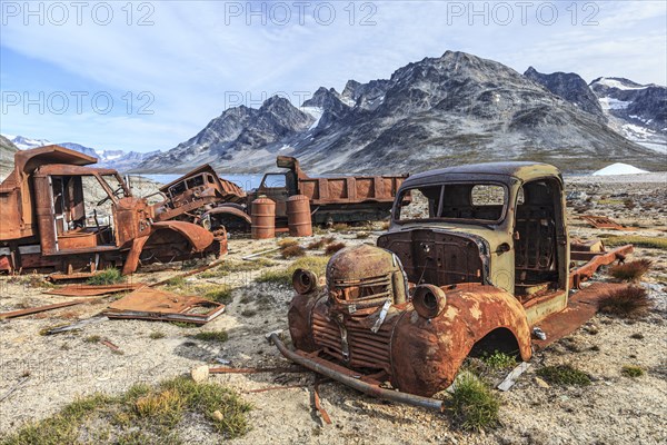 Rusty cars and oil drums in front of steep mountains, remains of a US airbase from the Second World
