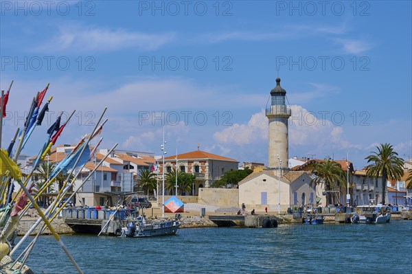 Coastal town with colourful houses and palm trees, boats in the water and a lighthouse, on a sunny