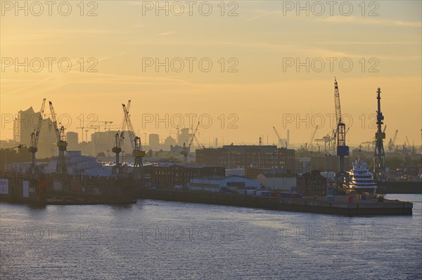 Harbour at sunrise, cranes rise into the sky, in the background buildings, Elbe Philharmonic Hall,