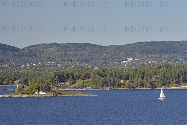 A lonely sailing boat near a small island, surrounded by water and with wooded hills in the