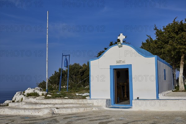 Profitis Ilias Chapel, White chapel with blue accents, surrounded by trees under a blue sky,