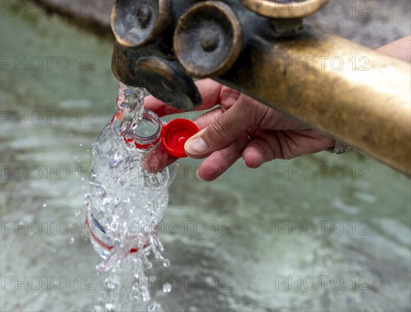 Water fountain, a woman fills drinking water into a small plastic bottle, Munich, Bavaria, Germany,