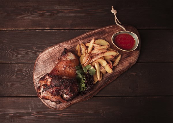 Pork knuckle, in soy-honey sauce, with fried potatoes, on a wooden chopping board, homemade, no