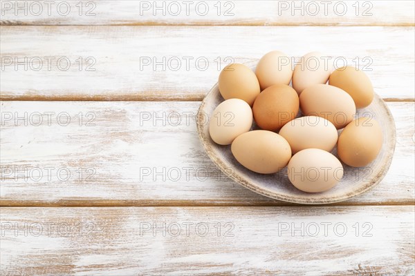 Pile of colored chicken eggs on plate on a white wooden background. side view, copy space, close up
