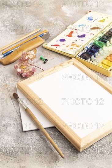 Drawing accessories set: brushes, pencils, watercolor, frame on brown concrete background. Side