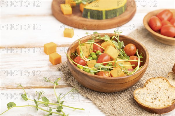 Vegetarian vegetable salad of tomatoes, pumpkin, microgreen pea sprouts on white wooden background