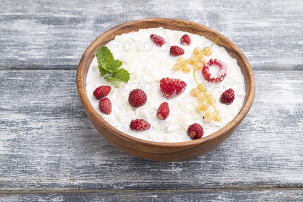 Rice flakes porridge with milk and strawberry in wooden bowl on gray wooden background. Side view,