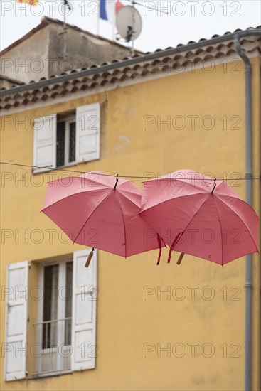 In the perfume town of Grasse, two red umbrellas hang between the houses, Grasse,