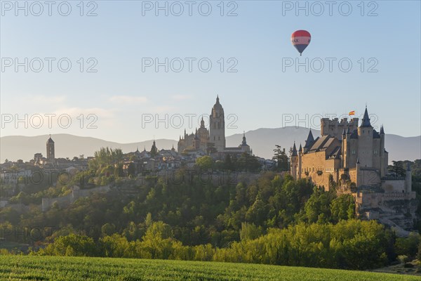 Beautiful view of a castle at sunrise with a hot air balloon in the sky and green fields in the
