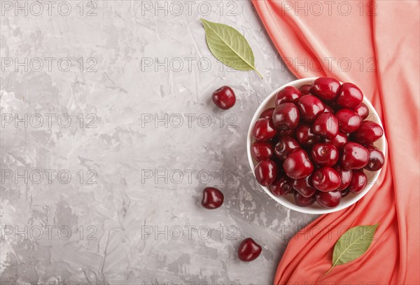 Fresh red sweet cherry in white bowl on gray background with red textile. top view, flat lay, copy