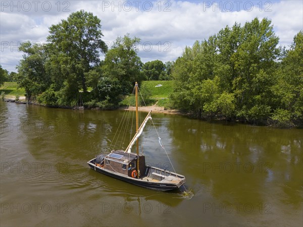 A lonely boat floats on a calm river, surrounded by green landscape and trees under a clear sky,