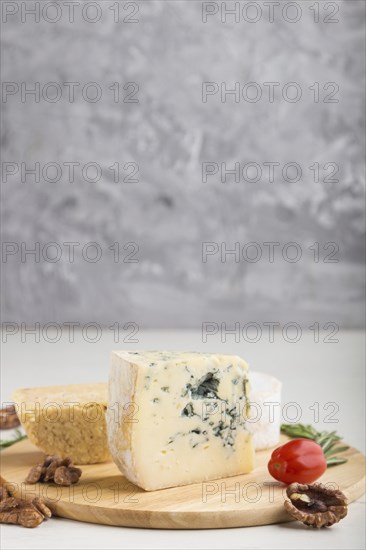 Blue cheese and various types of cheese with rosemary and tomatoes on wooden board on a white and