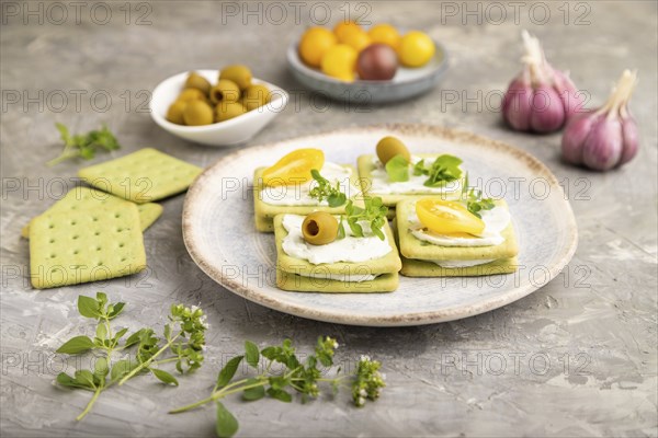 Green cracker sandwiches with cream cheese and cherry tomatoes on gray concrete background. side