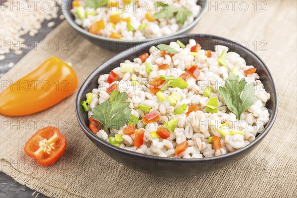 Pearl barley porridge with vegetables in blue ceramic bowls on a black concrete background and