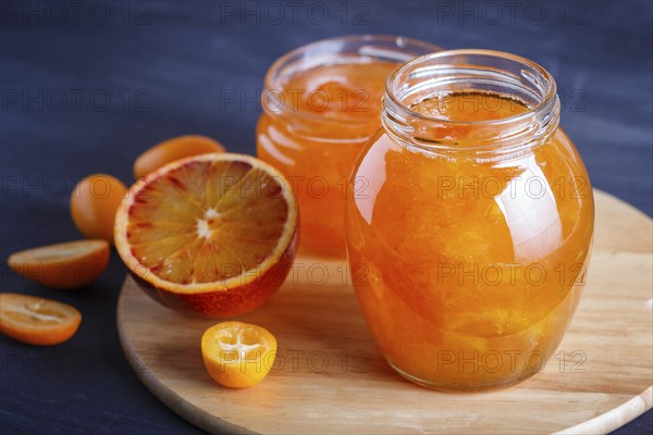 Orange and kumquat jam in a glass jar with fresh fruits on a wooden kitchen board. Homemade, close