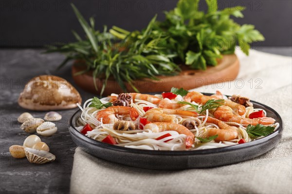 Rice noodles with shrimps or prawns and small octopuses on gray ceramic plate on a black concrete