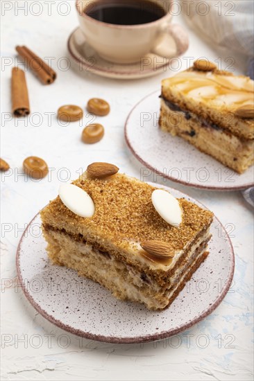 Honey cake with milk cream, caramel, almonds and a cup of coffee on a white concrete background and