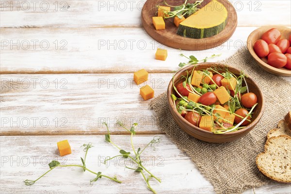 Vegetarian vegetable salad of tomatoes, pumpkin, microgreen pea sprouts on white wooden background