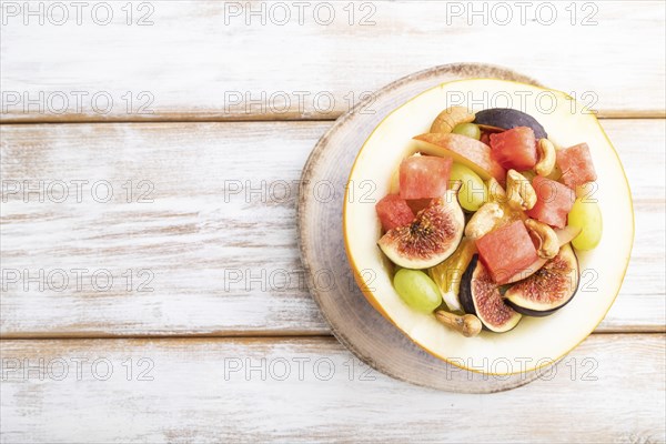 Vegetarian fruit salad of watermelon, grapes, figs, pear, orange, cashew on white wooden background