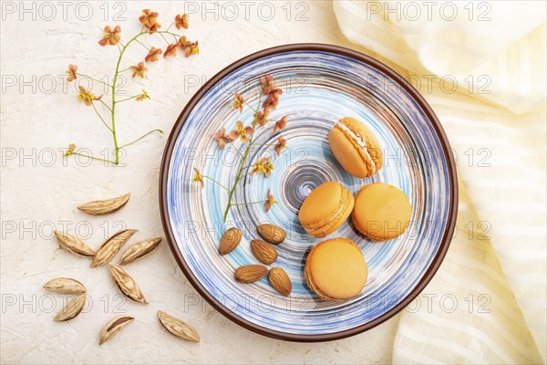 Orange macarons or macaroons cakes with cup of coffee on a white concrete background and linen