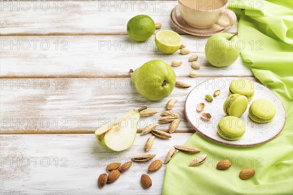 Green macarons or macaroons cakes with cup of coffee on a white wooden background and green linen