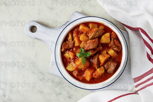 Potatoes stewed with meat, in tomato sauce, with spices and herbs, no people, on a white table