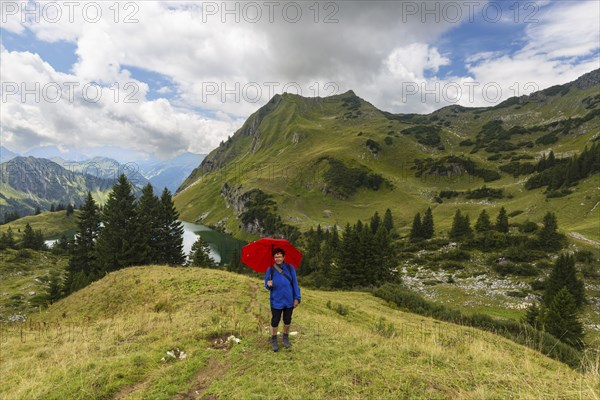 Woman 60-65 hiking with umbrella, behind her Seealpsee and Seeköpfel, 1919m, Allgäu Alps, Allgäu,