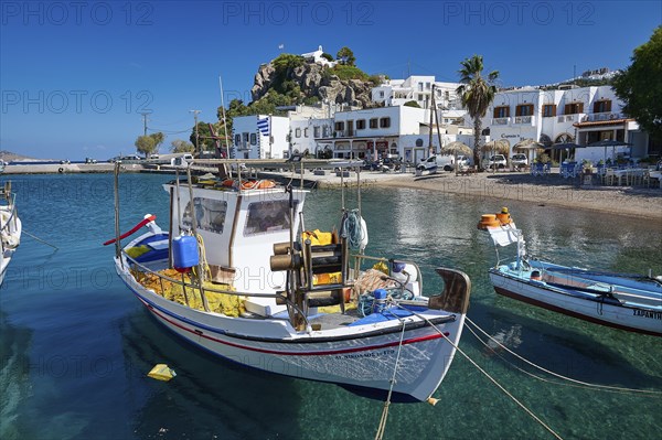 A white fishing boat moored at a Greek island harbour with crystal clear water and historic