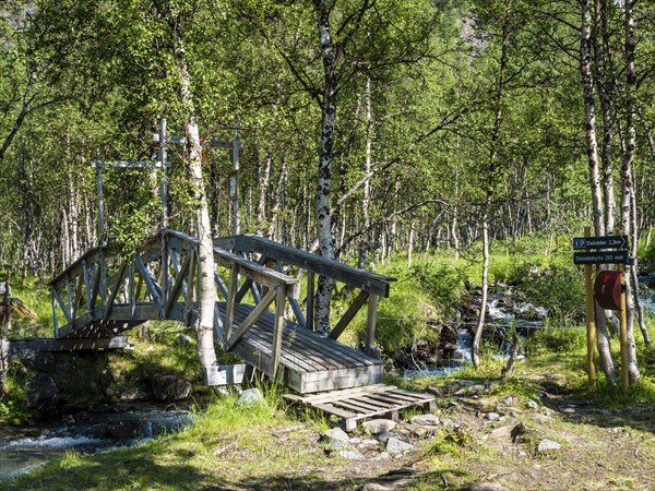 Wooden bridge on hiking path crosses a small river, hike along valley Steindalen to glacier
