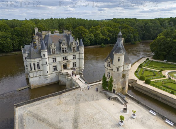 Renaissance castle with a tower and a bridge over a river, surrounded by green landscape, aerial