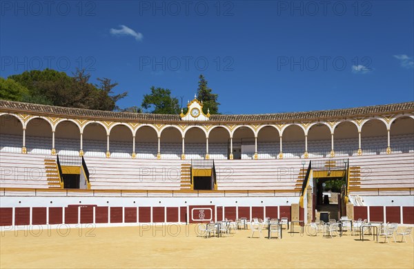 Historic bullring with classic architecture and blue sky, sandy floor and chairs in the centre,