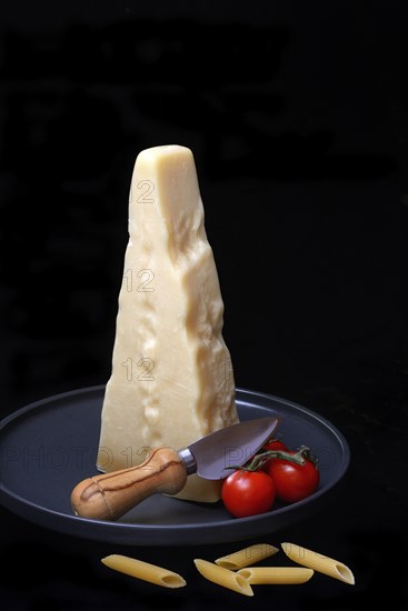 A piece of Parmesan cheese with cheese knife, pasta and tomatoes, Italy, Europe