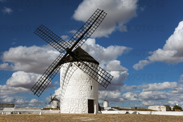 Historic white windmill under a blue sky with clouds and sunny surroundings in a wide landscape,