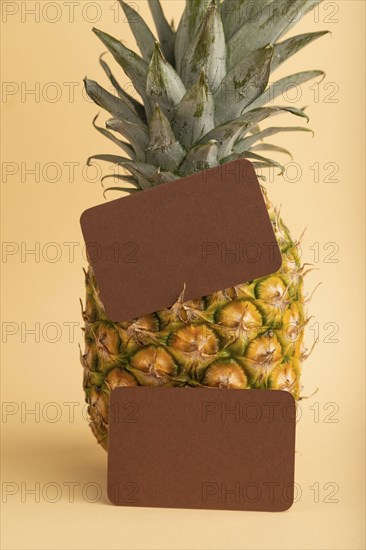 Brown paper business card with ripe pineapple on orange pastel background. Side view, copy space.