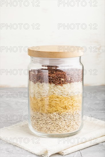 Glass jar with different kinds of rice poured in layers on a gray and white background. side view,