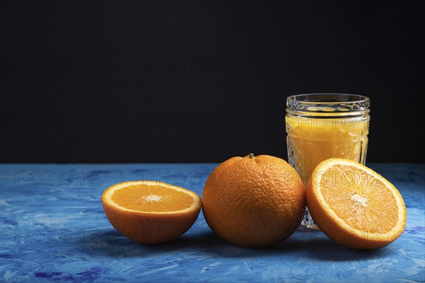 Glass of orange juice on a black and blue background. Hard light, contrast. Side view, copy space