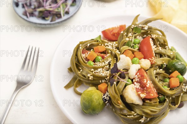 Tagliatelle green spinach pasta with tomato, pea and microgreen sprouts on a white wooden