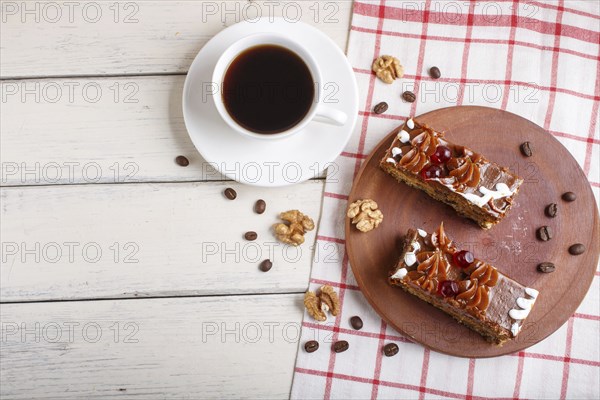A piece of cake with caramel cream on a wooden kitchen board and a cup of coffee, white background,