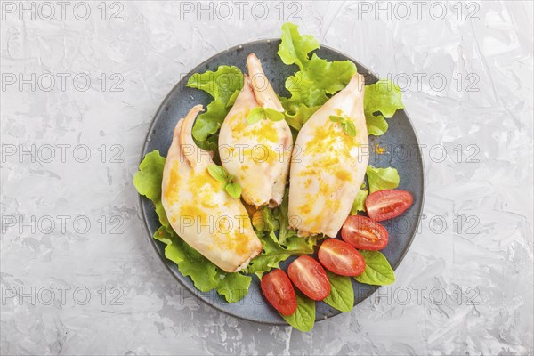 Stuffed baked squid with greens on a blue ceramic plate on a gray concrete background, top view,