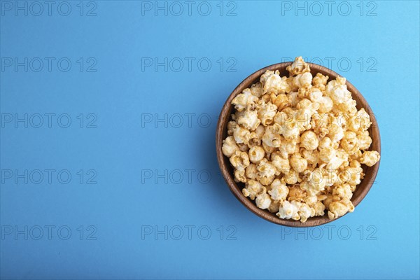 Popcorn with caramel in wooden bowl on a pastel blue background. Top view, flat lay, copy space