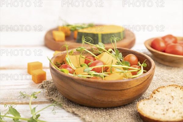 Vegetarian vegetable salad of tomatoes, pumpkin, microgreen pea sprouts on white wooden background